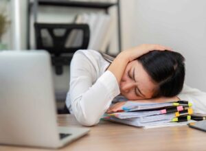 Stressed businesswoman asleep on a huge pile of landlord paperwork.
